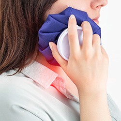 A woman placing a cold compress on her jaw