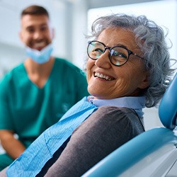 Woman with black glasses smiling while sitting in treatment chair