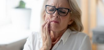 Older woman wincing and holding her cheek in pain