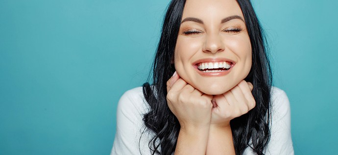 Woman with eyes closed grinning with hands under chin