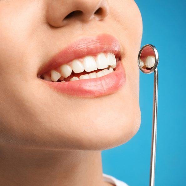 Nose-to-neck ¾ profile view of someone smiling with tooth reflected in dental mirror