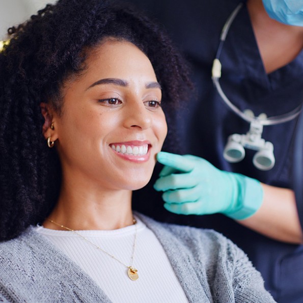 Woman in dental chair smiling into mirror with dentist touching her cheek