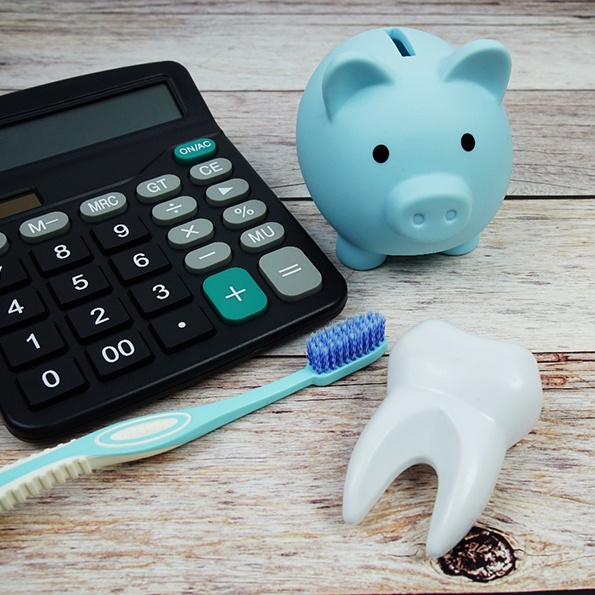 Blue piggy bank, toothbrush, calculator, and model tooth on wooden surface