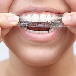 Fingers applying whitening strip to upper arch