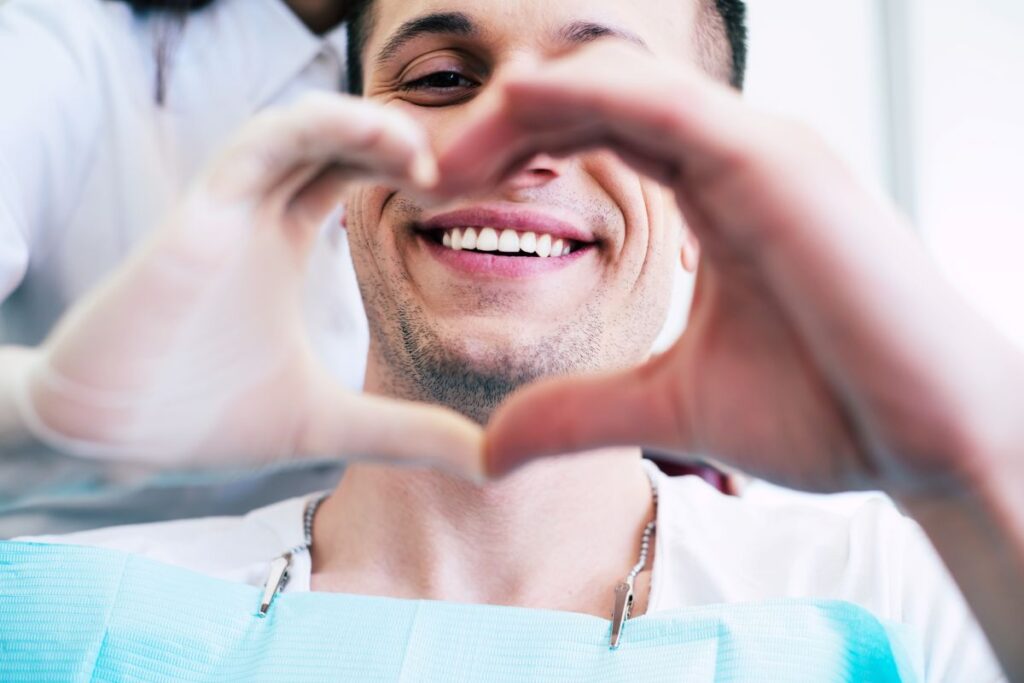 A happy man in a dental chair making a heart shape with his hands